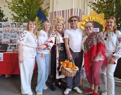 Des bénévoles en chemise brodée et couronne de fleurs posent avec un visiteur devant le grand tournesol du stand