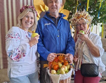 Un visiteur tenant un panier de pommes et de poires pose entre deux bénévoles en tenue ukrainienne