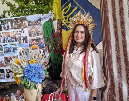Une bénévole coiffée d’une couronne d’épis et de rubans, à côté des bijoux en perles exposés sur le stand