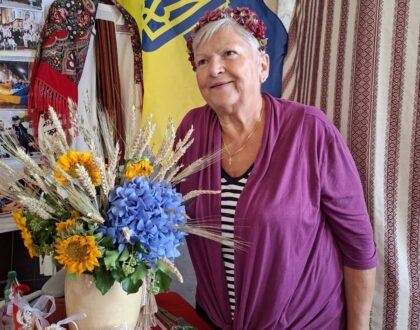 Une bénévole en gilet violet et couronne de fleurs devant le drapeau ukrainien et le bouquet du stand