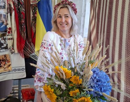 Une bénévole en chemise brodée et couronne de fleurs, assise derrière le bouquet de tournesols du stand
