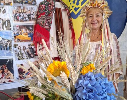Une bénévole en tenue traditionnelle et couronne d’épis devant le drapeau ukrainien, derrière un grand bouquet