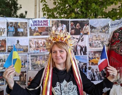 Une bénévole en couronne à rubans tient un petit drapeau ukrainien et un petit drapeau français devant le stand