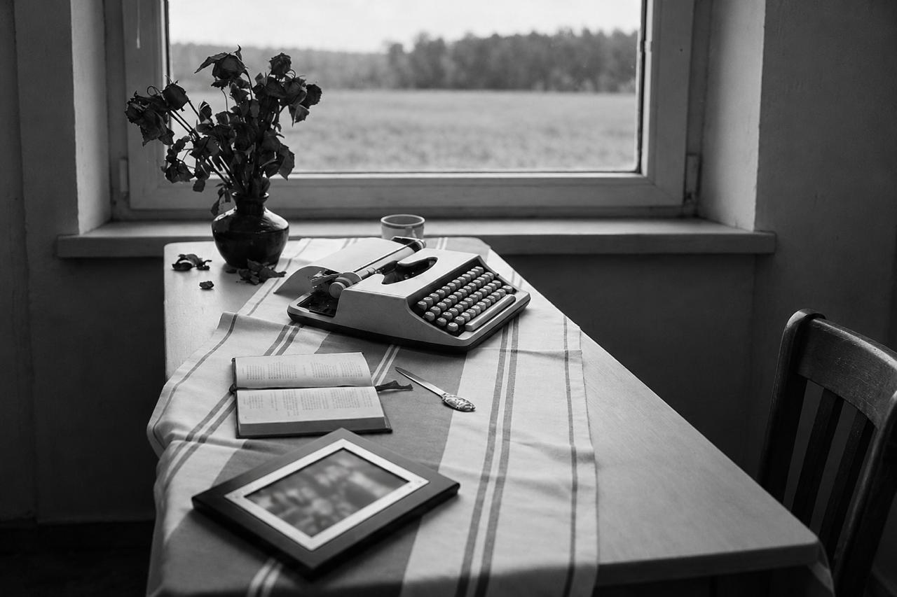 Machine à écrire, livre ouvert et photo encadrée sur une table près d’une fenêtre : projet littéraire « Essai » sur le thème « La guerre qui a changé ma vie »